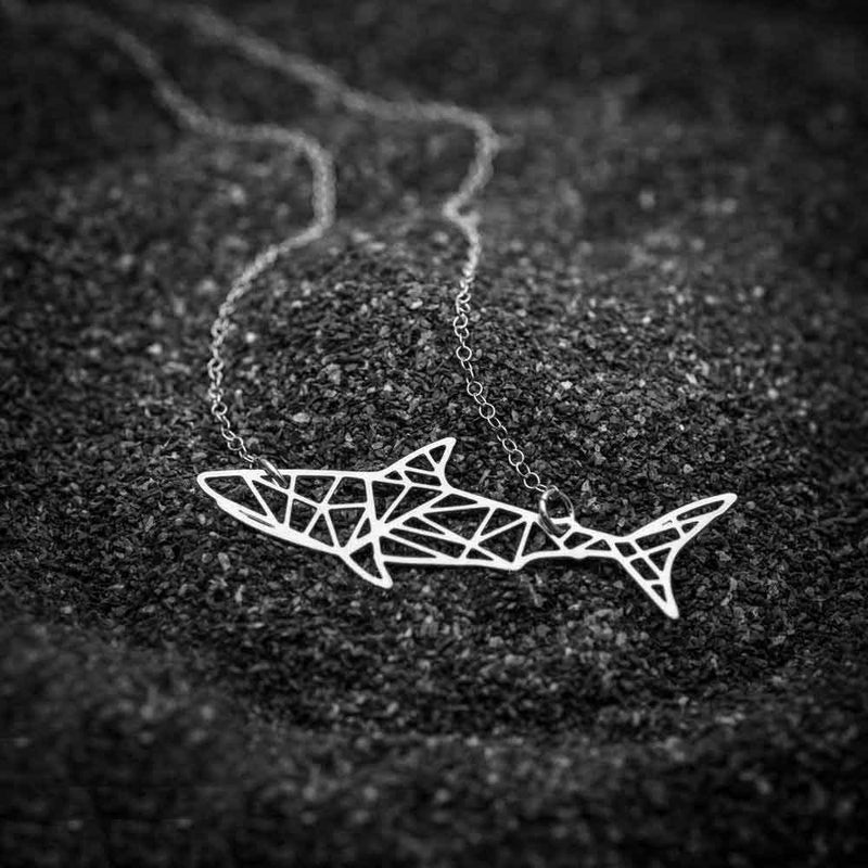 Laser cut shark pendant on black sand 