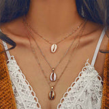 Gold Cowrie Shell Charm Necklace with three chains worn on woman 
