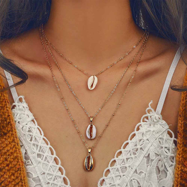 Gold Cowrie Shell Charm Necklace with three chains worn on woman 